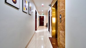 Un pasillo de hotel con obras enmarcadas en las paredes, suelo de mármol y puerta de ascensor dorada.