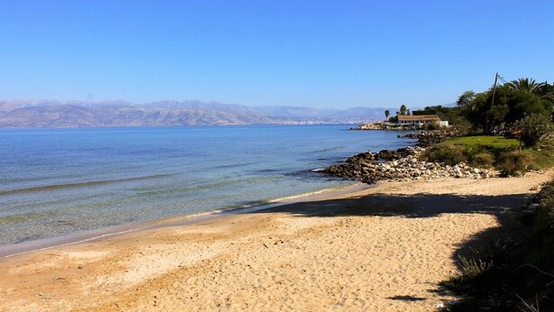 A beach with clear water, a rocky shoreline, and a house on a hill with a view of the sea. - Spacious two-bedroom apartment near sandy beach (Corfu)