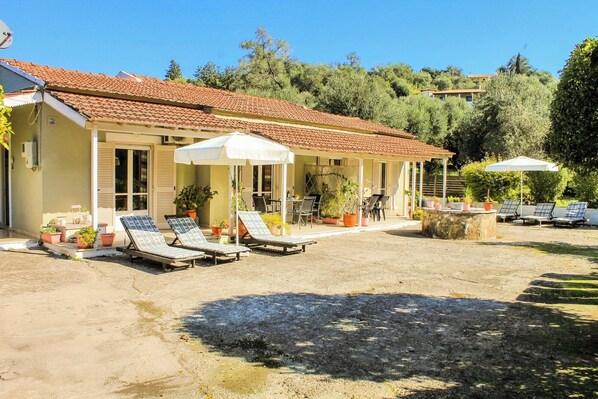 A building with a tiled roof, outdoor seating with umbrellas, and potted plants. - Spacious two-bedroom apartment near sandy beach (Corfu)