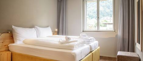 A neatly made bed with white linens, a wooden headboard, and a window with curtains.