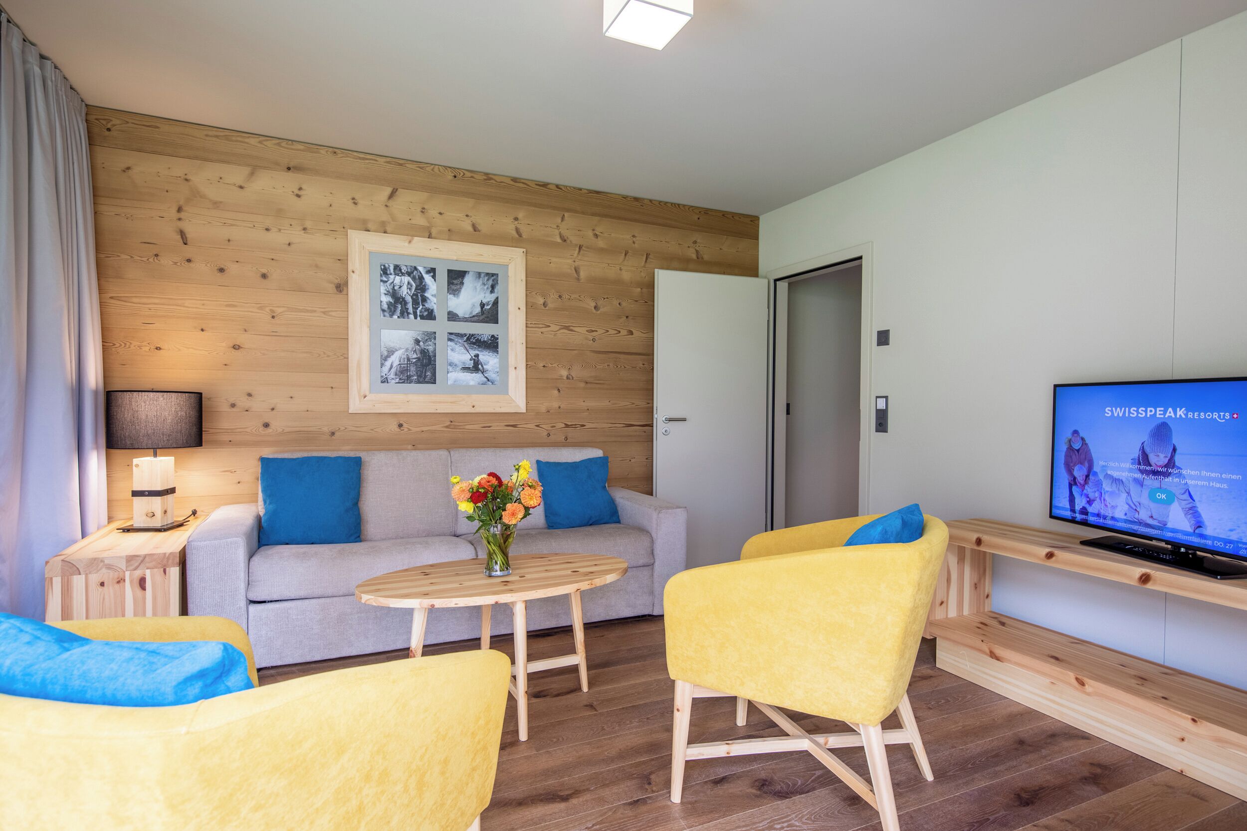 Une pièce moderne avec un canapé, des fauteuils jaunes, un téléviseur et un mur en bois.
