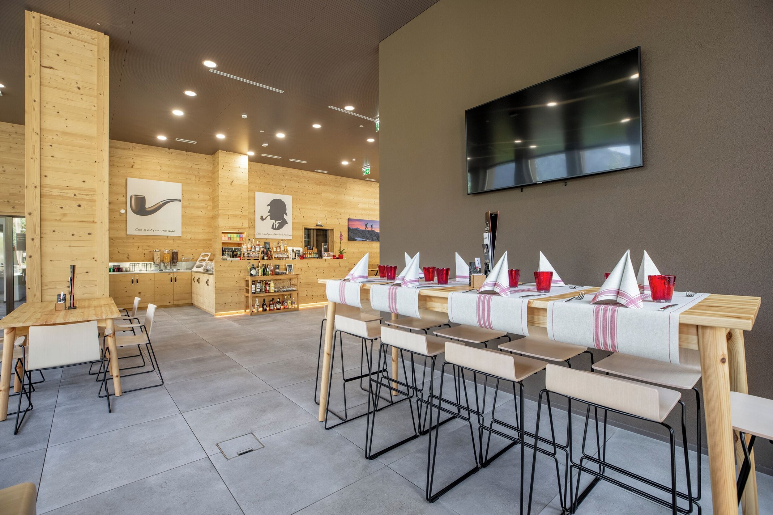 Un restaurante moderno con paredes de madera, una televisión de pantalla plana y varias mesas con vasos rojos.