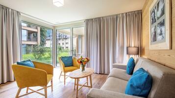 A modern living room with a sofa, armchairs, a small table, and a view of the outdoors.