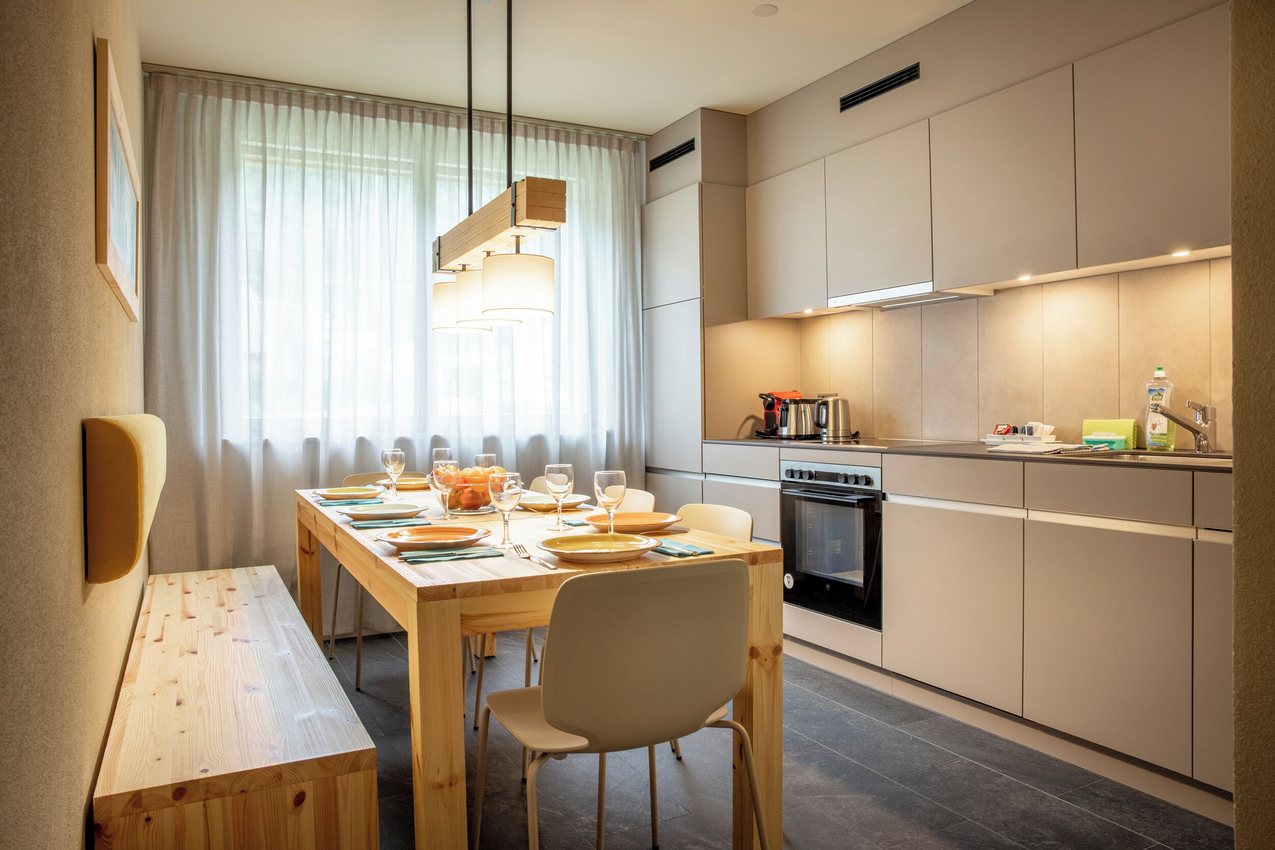 A modern kitchen with a dining area, featuring a wooden table, chairs, and a built-in oven.