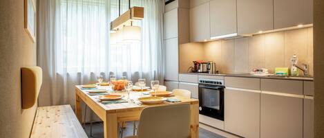 A modern kitchen with a dining area, featuring a wooden table, chairs, and a built-in oven.
