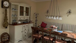 A dining area with a wooden table, chairs, a white cabinet with glass doors, a clock, and a hanging light fixture.