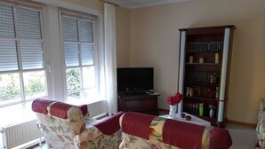 A living room with a sofa set, a television, a bookshelf, and a window with blinds.