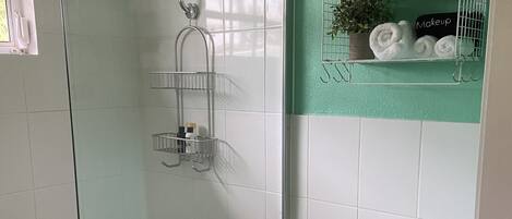 A bathroom with a glass-enclosed shower, a toilet, and a shelf with towels and toiletries.