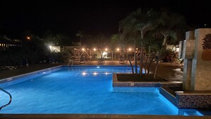 A nighttime swimming pool with a clear water surface, surrounded by palm trees and a covered seating area with lights. - New listing! Easy walk to 3 separate Beaches, Pool, and multiple Restaurants! (St thomas)