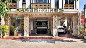 La entrada del HOTEL BUCHEU 2, con fachada de mármol, un coche estacionado y un cartel con texto.