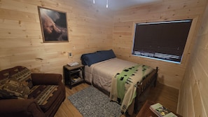 Una habitación acogedora con una cama, cabecero de madera, una mesita de noche, alfombra estampada y un cuadro colgado en la pared.