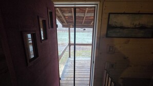 Een kamer met uitzicht op een omheind terras, een houten deur en een lijst met een afbeelding aan de muur.