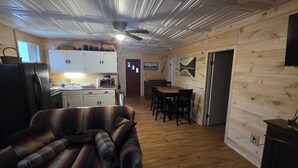 Een knus blokhutinterieur met keuken, eethoek en woonkamer met een geruit bankje.