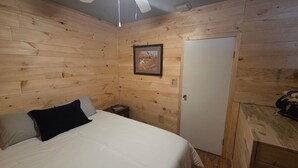 Een kamer met houten lambrisering, een bed, een lijst met een afbeelding en een deur.