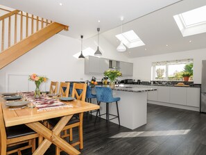 A modern kitchen with a central island, a dining area with wooden furniture, and a staircase leading to an upper level. - Zephyr (Helston)