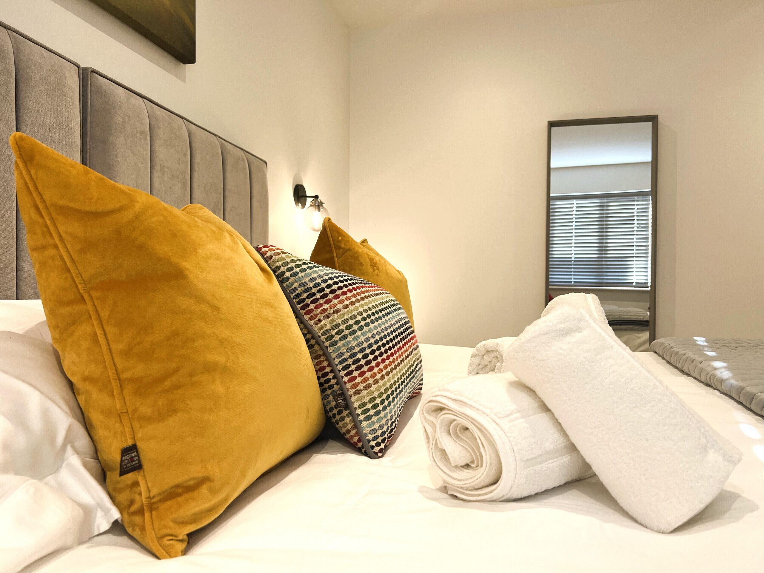 A neatly made bed with a headboard, multiple pillows, and a rolled-up towel.