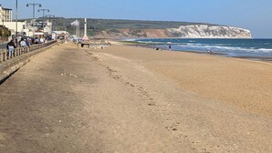 A coastal beach with a promenade, cliffs, and a clear sky. - Laurel Cottage (Newchurch)