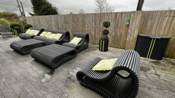 A patio area with three black lounge chairs with yellow cushions, a small potted plant, and a trash bin.
