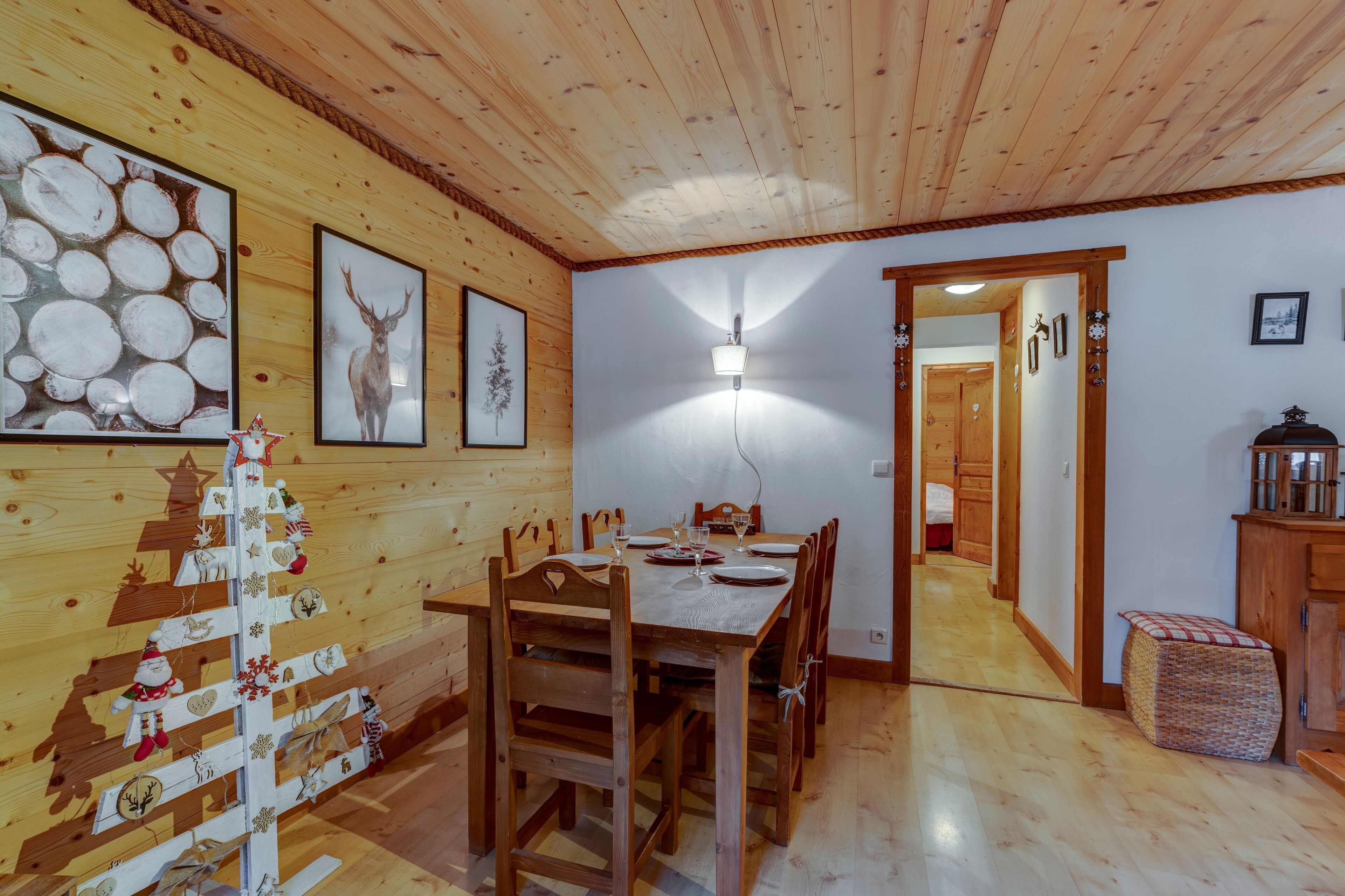 Un coin repas en bois avec une table dressée pour six personnes, une décoration de Noël et un couloir menant à une autre pièce.