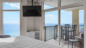 Een slaapkamer met een groot bed, een aan de muur bevestigde televisie en een balkon met uitzicht op zee.