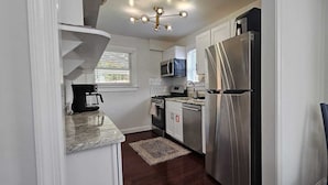 A modern kitchen with a stainless steel refrigerator, a microwave, and a stove. There is a coffee maker on the counter and a chair in the corner. - Short Walk to Metro - Fenced Yard + Covered Patio (Silver Spring)
