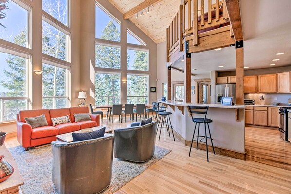 A spacious living area with a large window, a red sofa, and a kitchen with wooden cabinets and a bar area.