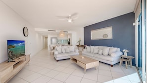 A modern living room with a sofa set, a coffee table, a TV, and a dining area. - C Bargara Unit 101 Ocean Front (Bargara)
