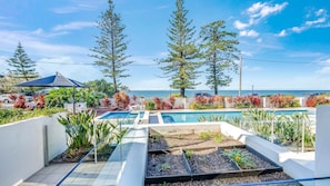 A pool area with a view of the ocean, surrounded by plants and trees. - C Bargara Unit 101 Ocean Front (Bargara)