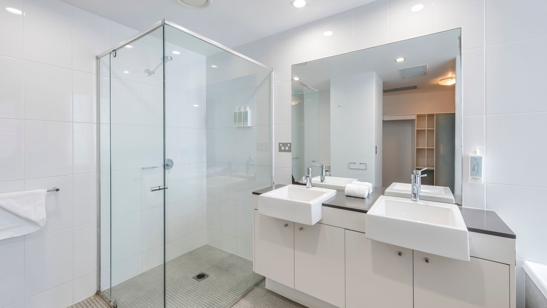 Ein modernes Badezimmer mit einer begehbaren Glasdusche, zwei Waschbecken und einem großen Spiegel.