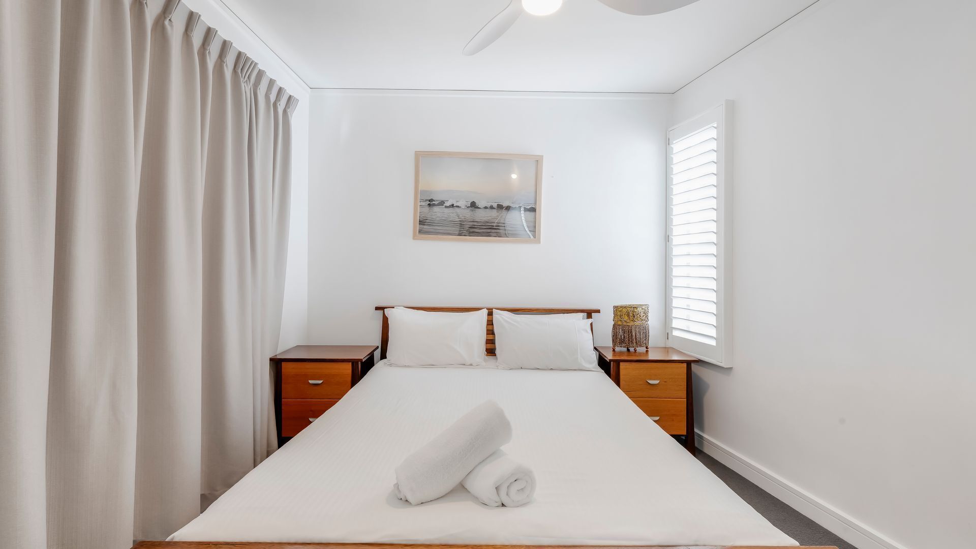 Une chambre d’hôtel avec un grand lit, deux tables de chevet, un tableau au mur et une fenêtre avec des stores.