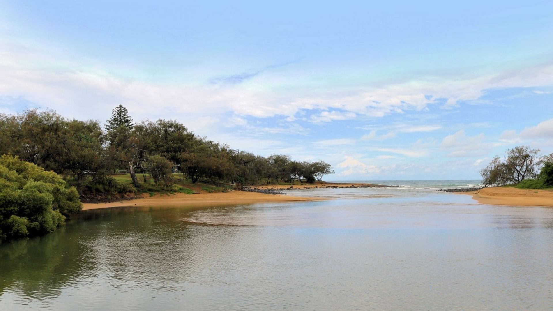 Une rivière paisible, bordée d’une plage de sable et d’une végétation dense.