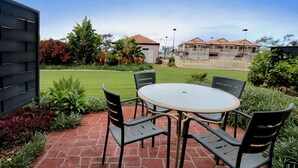 A patio with a round table and four chairs, surrounded by a brick pathway and various plants.