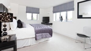 A modern bedroom with a bed, a TV, a desk, and a chair.