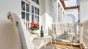 A balcony with wicker chairs, a table with a bottle and glasses, and a potted plant with red flowers. - Penthouse Apt, La Cala de Mijas Close to the Beach (Mijas Costa)