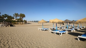 A beach with sun loungers and thatched umbrellas, palm trees, and a clear sky. - Penthouse Apt, La Cala de Mijas Close to the Beach (Mijas Costa)