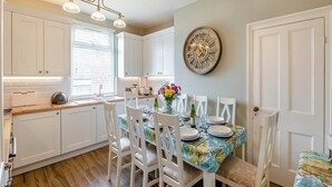 A modern kitchen with white cabinets, a dining table set for four, and a large wall clock.