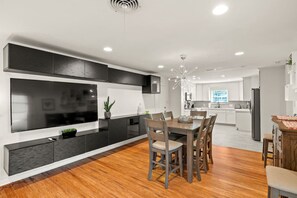 Una cucina moderna con zona pranzo, dotata di un ampio televisore a schermo piatto, mobili scuri e un tavolo da pranzo in legno con sedie.