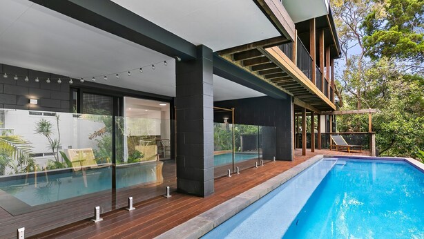 Une maison moderne dotée d’une piscine, de grandes baies vitrées et d’une terrasse en bois.