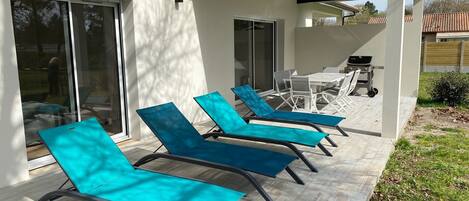 A patio with four blue lounge chairs, a table, and a grill.