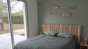 A bedroom with a large bed, a wooden headboard, a bench, and two wooden paddles on the wall. - Cottage Chaleureux Proche de L'océan (Grayan-et-l'Hôpital)