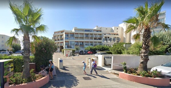 Un edificio residencial de varios pisos con balcones, rodeado de palmeras y coches aparcados.