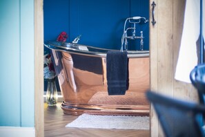 A bathtub with a towel, a vase with flowers, and a wooden floor. - Brandy Cove - 1 Bed Cabin - Landimore (Swansea)