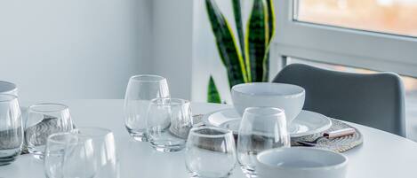 Una mesa redonda blanca dispuesta con cristalería transparente y platos blancos, junto con individuales tejidos y una ramita de canela.