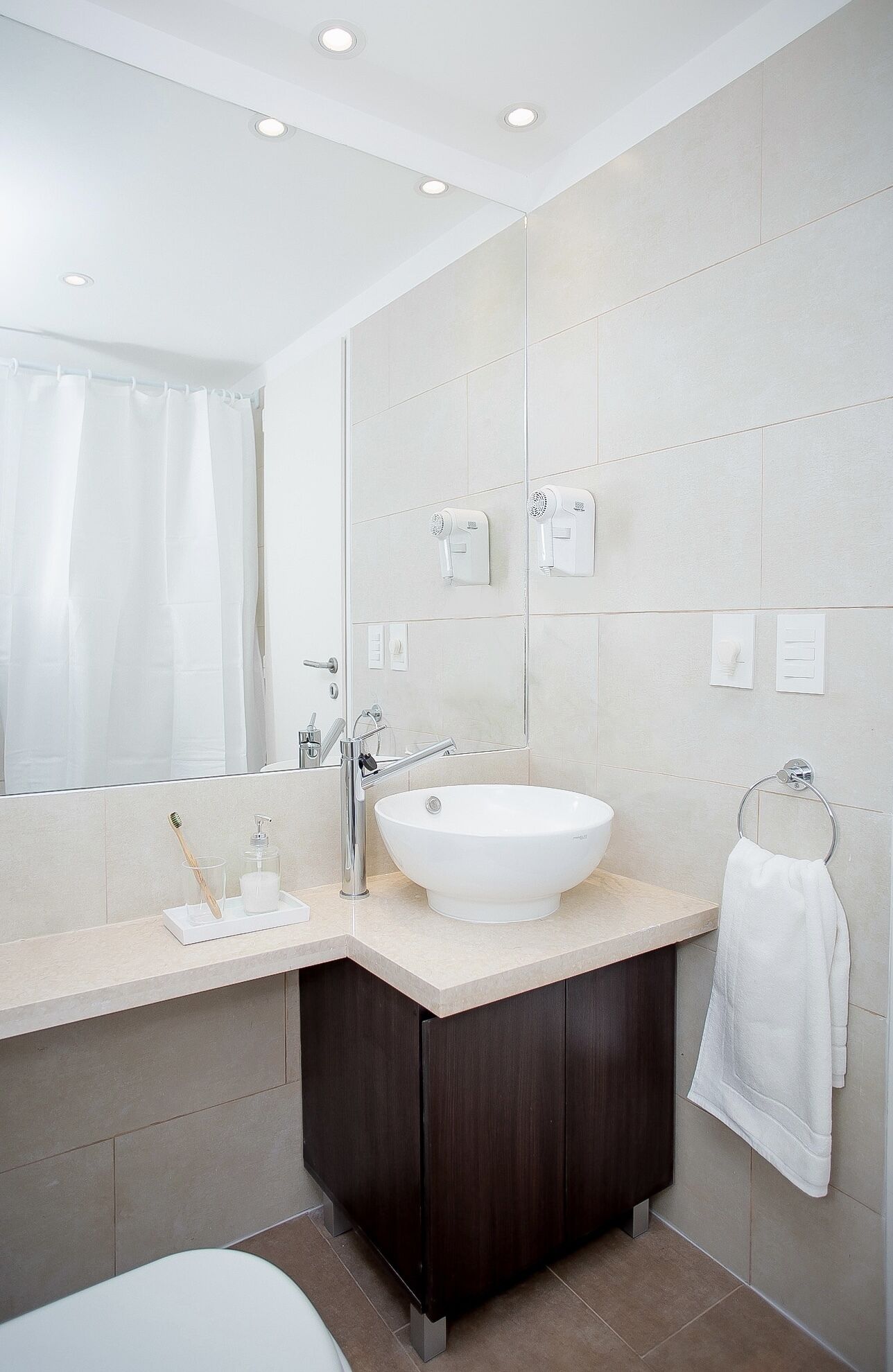 A modern bathroom with a large mirror, a white sink, and a dark wooden cabinet.