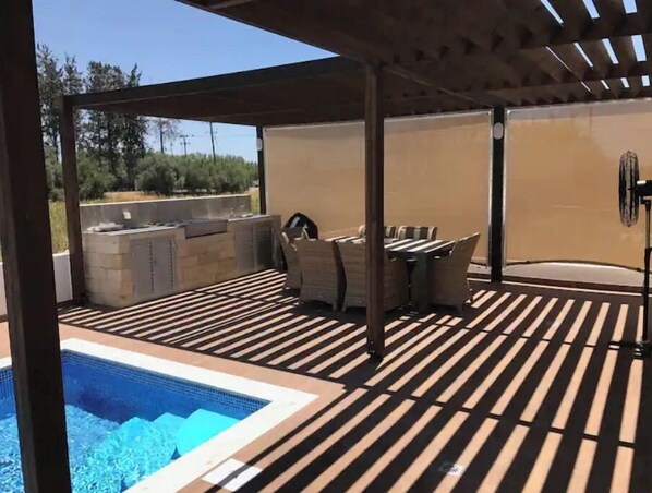 Un espacio al aire libre techado con piscina, terraza de madera y mobiliario exterior.