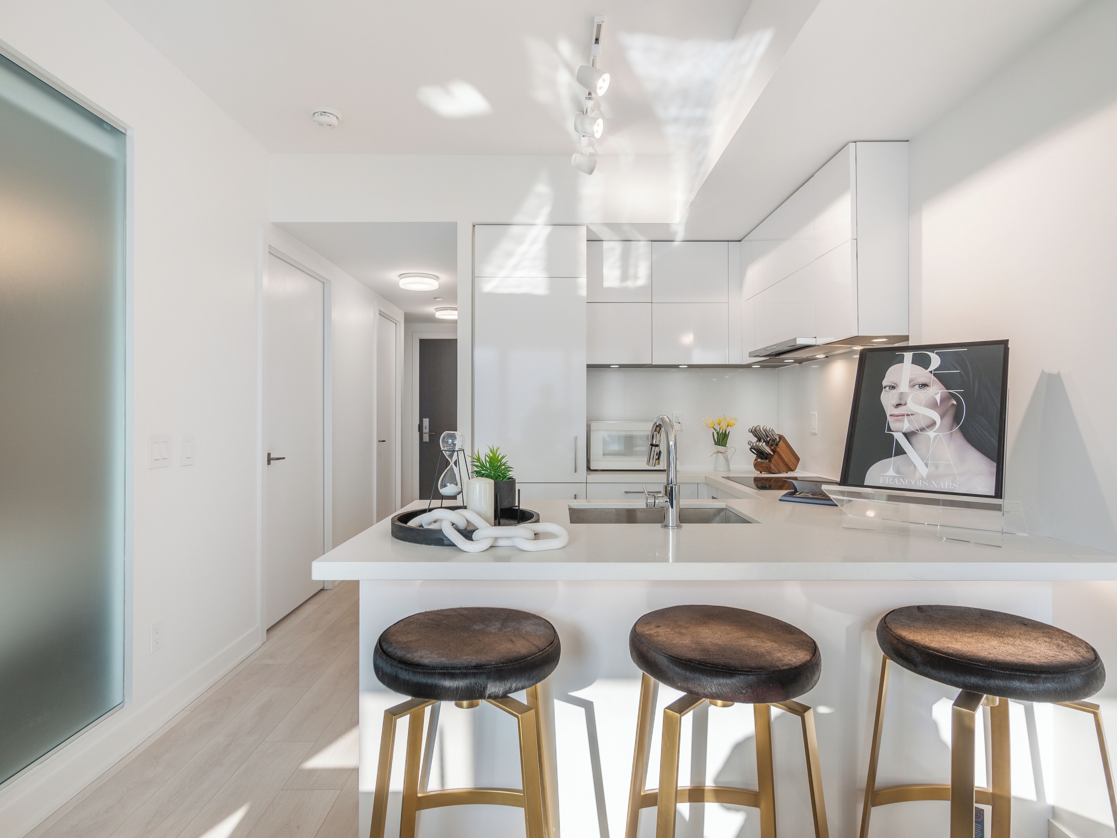 Una cocina moderna con una isla central, taburetes de bar y una obra enmarcada en la pared.