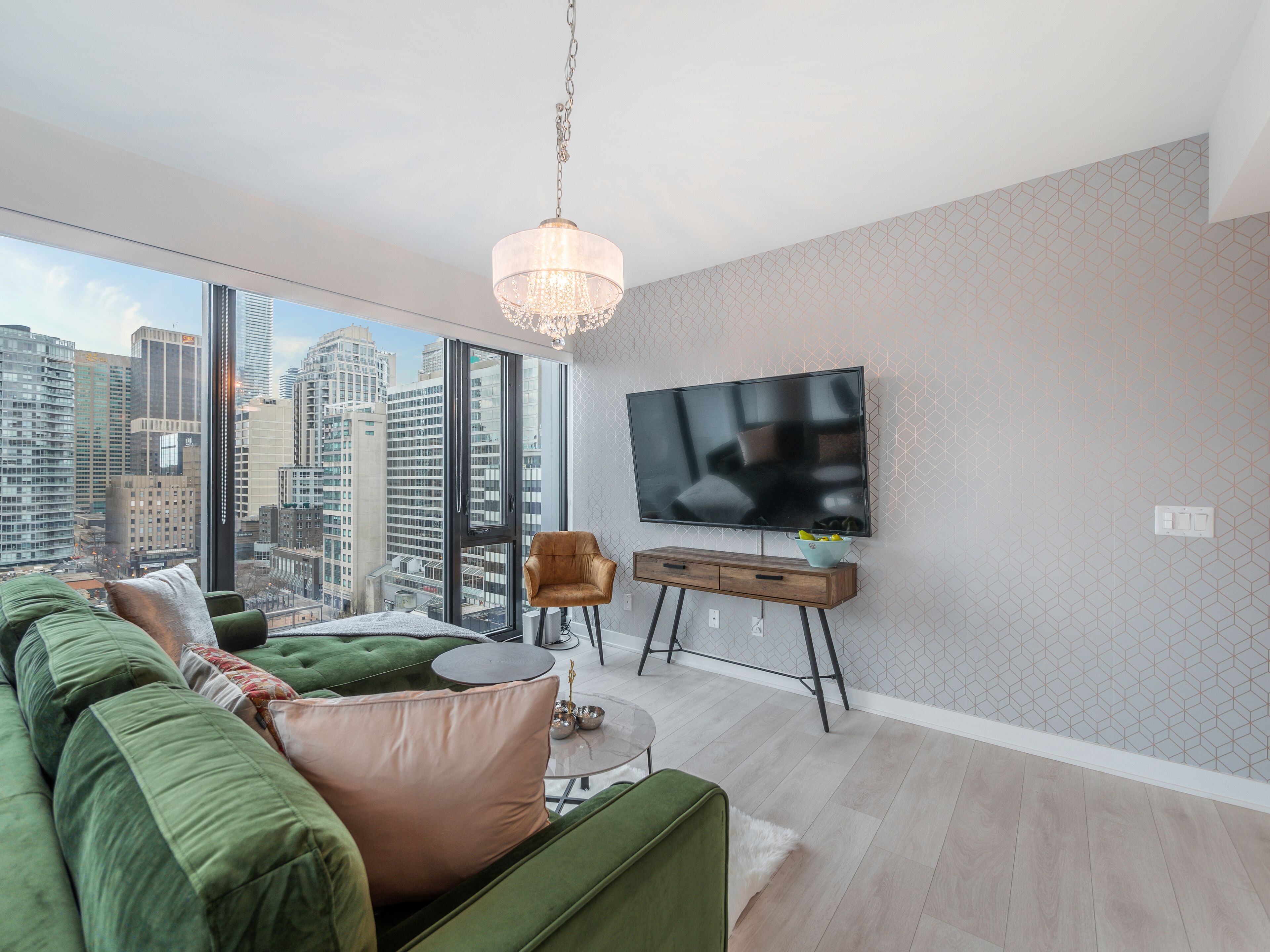 Una sala de estar moderna con un ventanal grande, un sofá verde, un televisor sobre un mueble bajo y vistas a la ciudad.