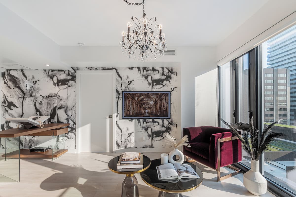 A modern living room with a marble wall, a chandelier, a red sofa, and a large window offering a city view.