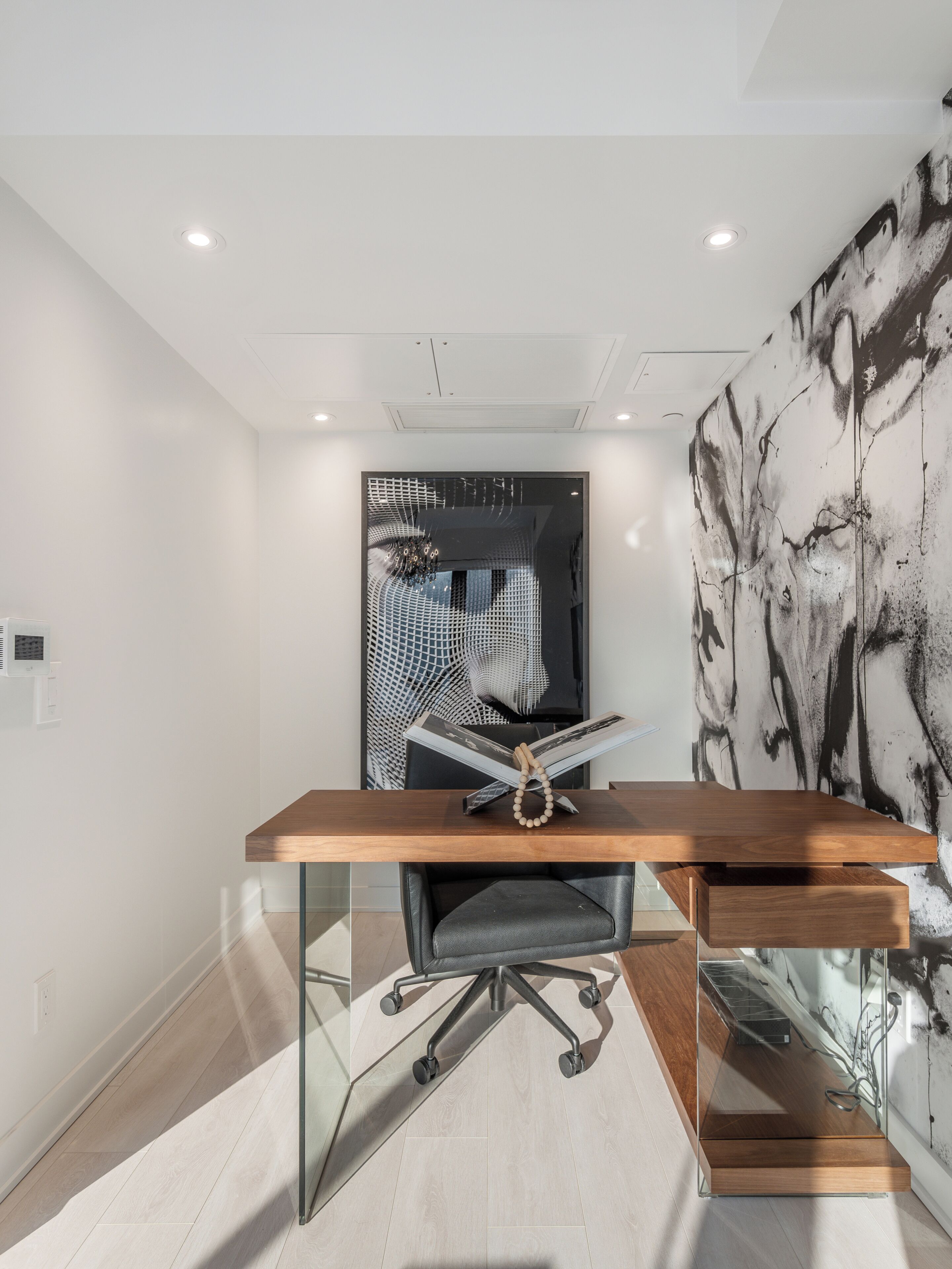 A modern office space with a wooden desk, a black office chair, and a glass partition.