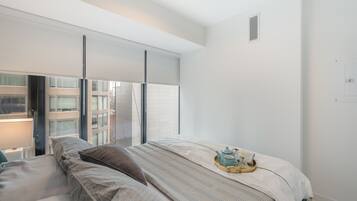Ein modernes Schlafzimmer mit einem großen Bett, einem Nachttisch und einem Fenster mit Blick auf Gebäude.